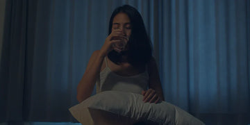 young woman sitting on bed drinking water