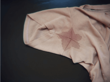 Close-up of a beige shirt showcasing a visible underarm sweat stain on a dark background