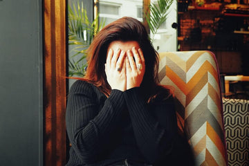 Woman covering her face while seated in a patterned chair indoors