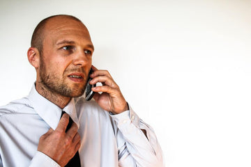 Man in a white dress shirt talking on a phone while adjusting his collar against a white background