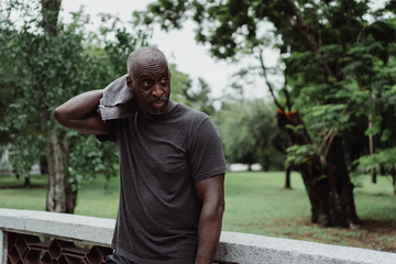 Man wiping sweat from his neck with a towel while wearing a dark shirt outdoors