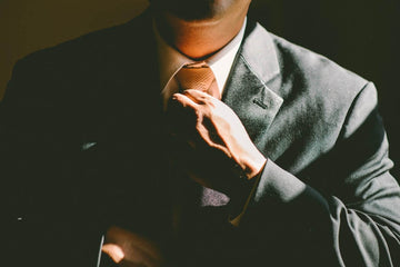 Man adjusting his tie while wearing a gray suit and white dress shirt