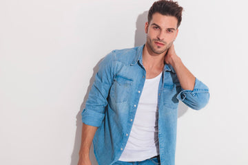 Man wearing a white undershirt beneath an open denim shirt against a white wall