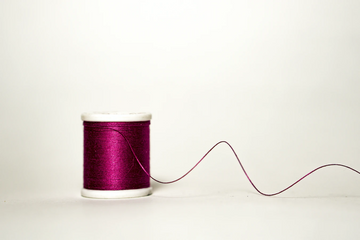 Spool of magenta thread with loose thread trailing across a white background