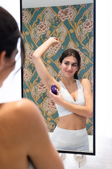 Woman applying an underarm product while looking in a bathroom mirror
