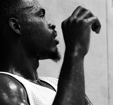 Sweating man in a tank top raising his arm near his face in a black-and-white portrait