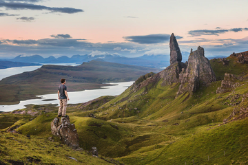 Man standing on a rocky outcrop overlooking a mountainous landscape and lake