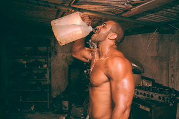 Man drinking water from a large container in a dim rustic setting, illustrating hydration