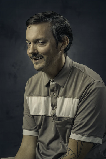 Man wearing a gray and cream polo shirt against a dark background