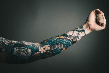 Side view of a tattooed arm showcasing colorful floral and fish designs against a dark background