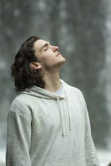 Man practicing mindful breathing with eyes closed while wearing a light gray hoodie