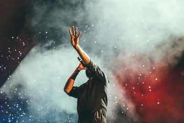 Person raising their arms amid colorful smoke and stage lighting