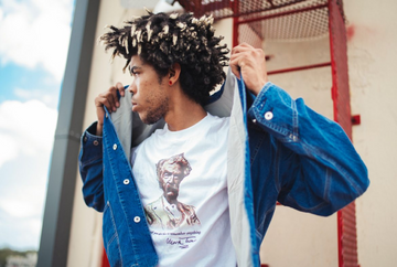 Man putting on a blue denim jacket over a graphic white T-shirt outdoors