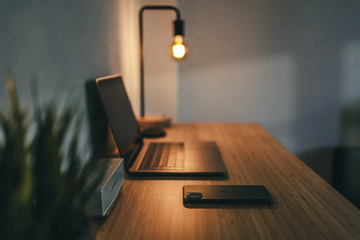 Laptop and smartphone on a desk beside a lamp in a softly lit workspace