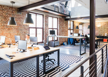 Employees working at computers in a bright, brick-walled open-plan office
