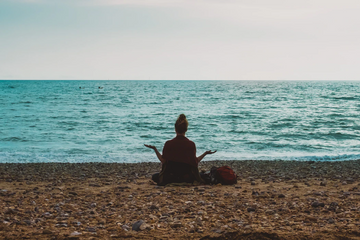 Person meditating on a rocky beach facing the sea