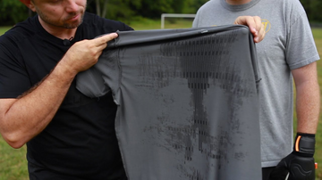 Two men hold a gray shirt showing dark moisture marks during a moisture absorption demonstration