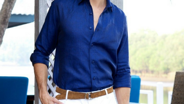 Person wearing a dark blue button-down shirt with rolled sleeves and white pants outdoors