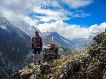 Hiker standing on a rocky mountain trail overlooking snow-capped peaks