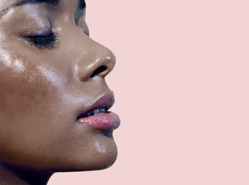 Close-up profile of a Black woman with a visibly sweaty face against a pale pink background