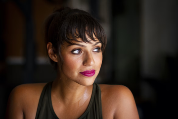 Woman with visible perspiration wearing a dark sleeveless top against a dark background