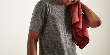 Person in a gray shirt drying their neck with a red towel against a light background