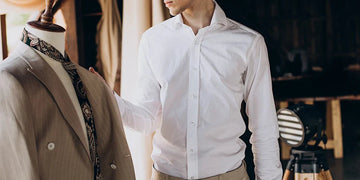 Man in a white dress shirt adjusts a suit jacket on a mannequin in a clothing studio
