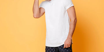 Man wearing a white summer undershirt and patterned shorts against an orange background