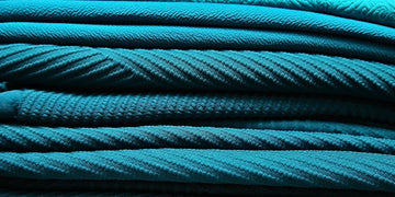 Close-up of stacked turquoise fabrics showcasing varied woven textures on a dark background