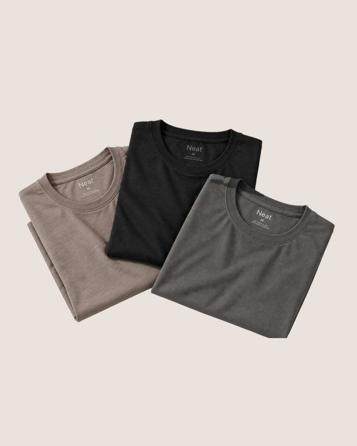 Mocha, Black and Stone Grey Neat crew necks folded and overlapping on a warm beige background