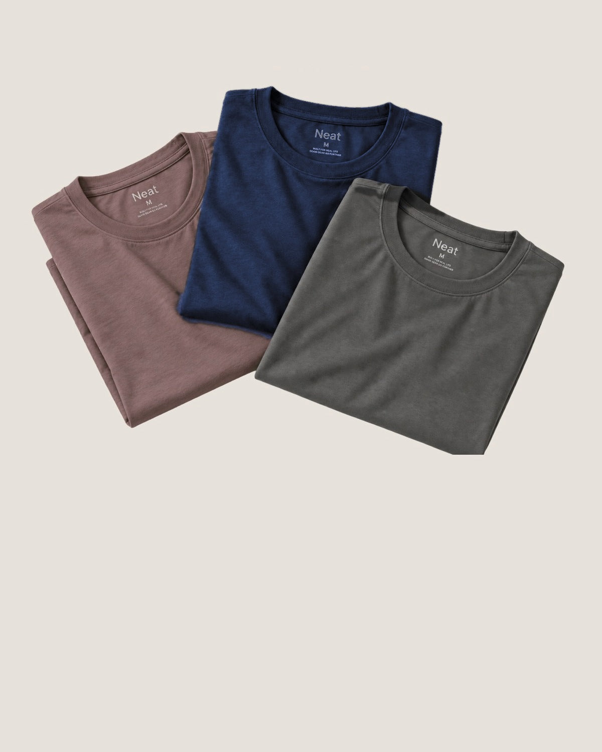 Dusty Clay, Deja Blue and Stone Grey Neat crew necks folded and overlapping on a warm beige background